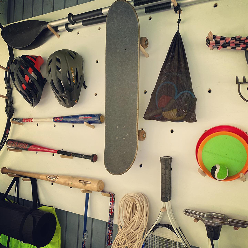 A large white outdoor wooden pegboard filled with sports equipment