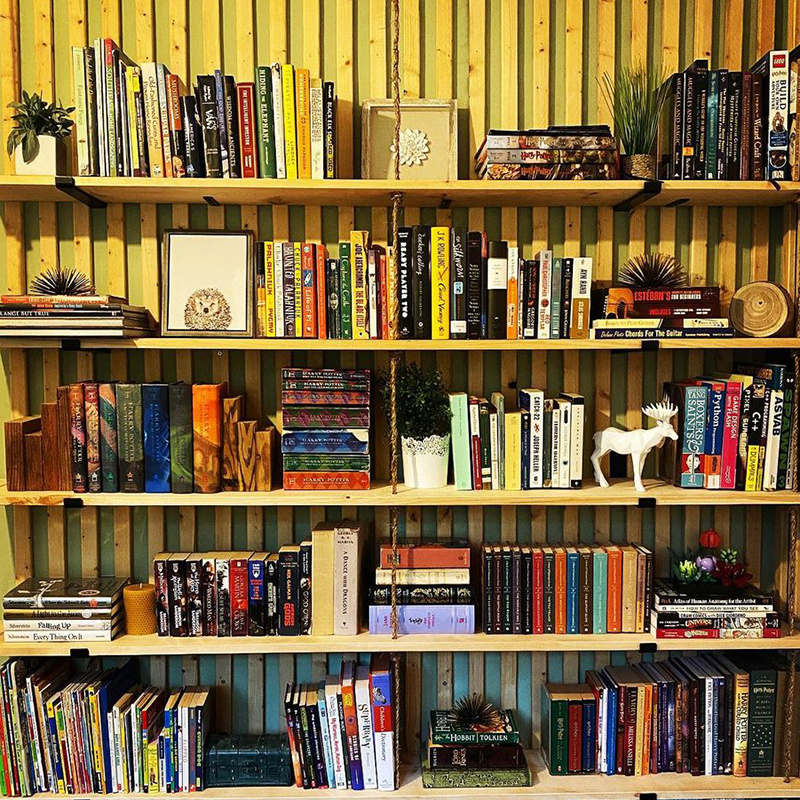 Wooden slat wall bookshelves filled with books and decorative items against a green wall